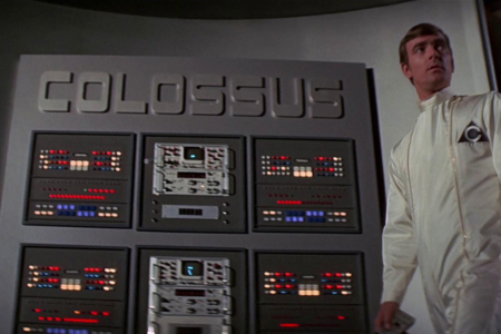 <p><strong>Figure 2.1</strong> When Forbin pauses at a large control panel to make adjustments, we glimpse the triangular logo on his white cleansuit, and in the background, the logotype for Colossus.</p>
