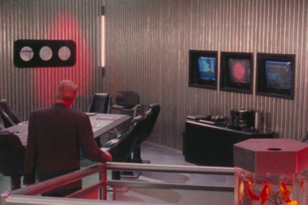 <p><strong>Figure 4.1</strong> The Federal Colonies logo can be seen on a wall monitor to the right, as Richter and Cohaagen enter the conference area.</p>