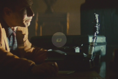 <p><strong>Figure 1.2</strong> As Deckard begins to question Rachel, we can see the V-K logo on the case in the background, in the highlighted area.</p>