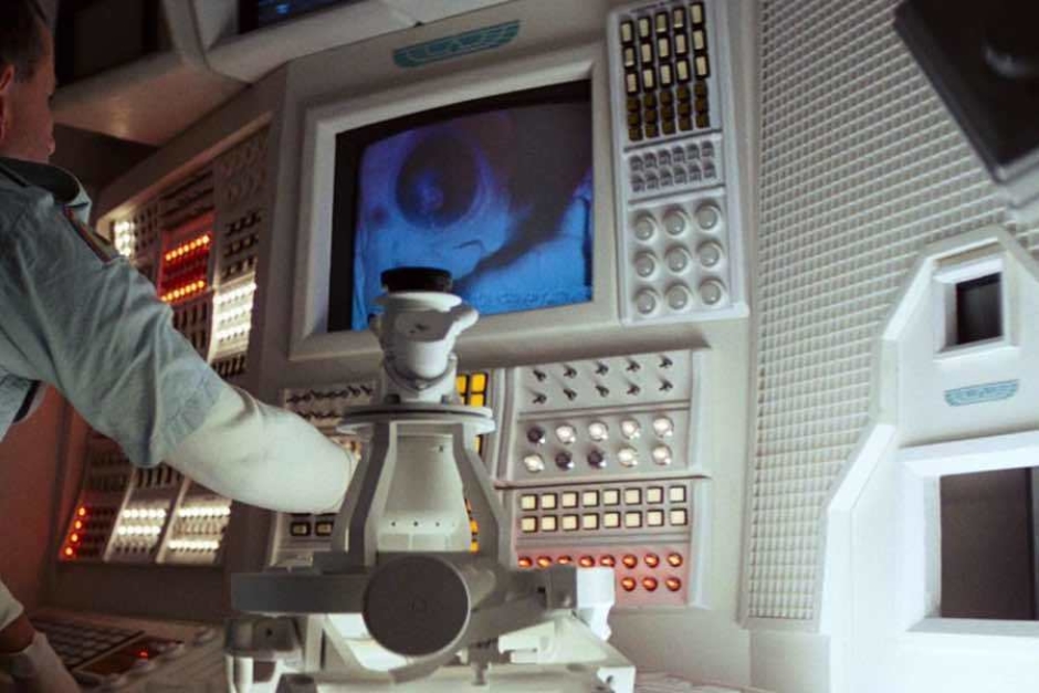 <p><strong>Figure 2.4</strong> At Ash’s lab terminal in the ship’s infirmary, we see the logo above screen displays (top center and center right).</p>
